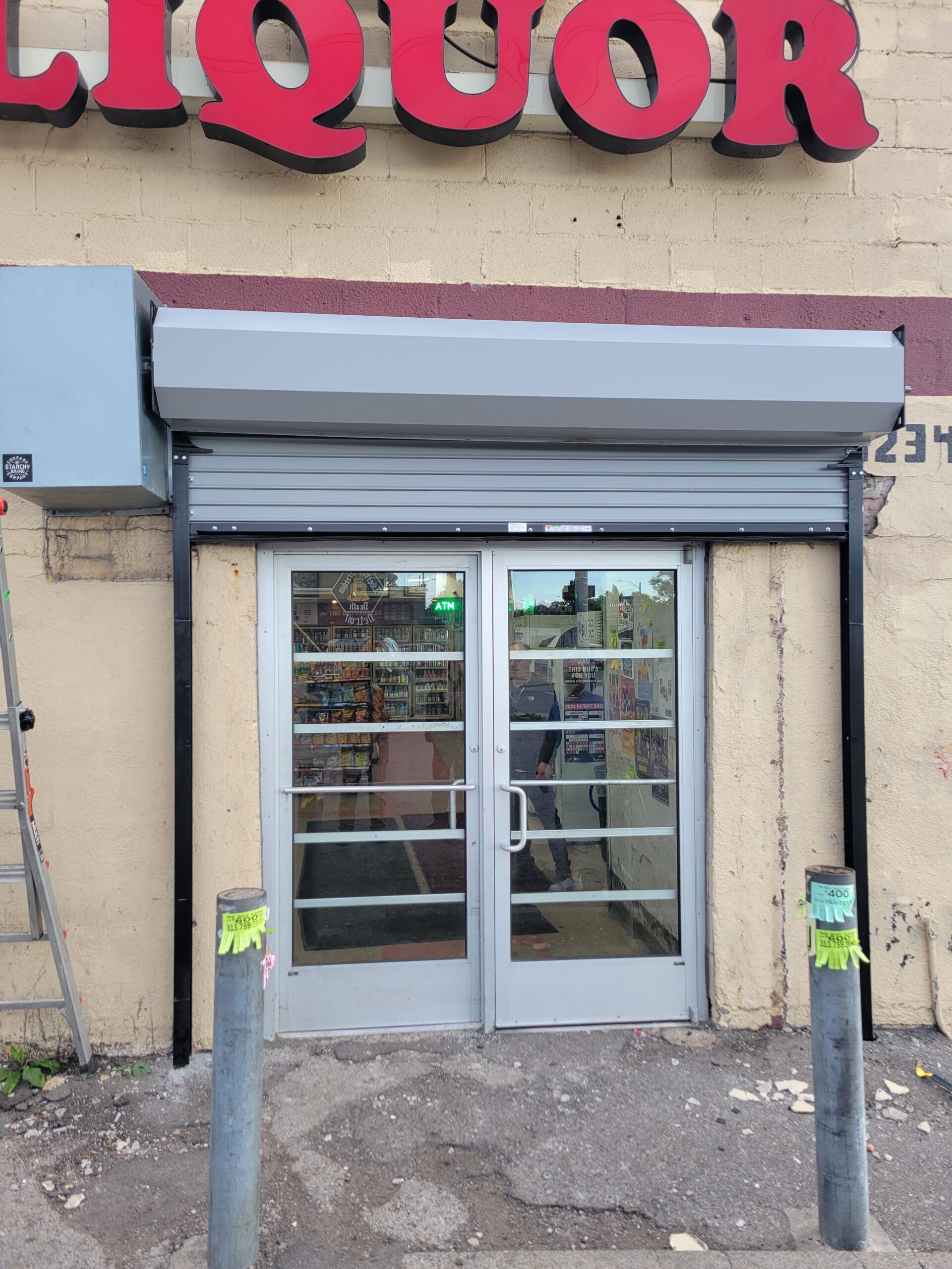 Glass double doors at the entrance of a liquor store, with part of the red LIQUOR sign visible above and a glimpse of the store’s interior through the doors.