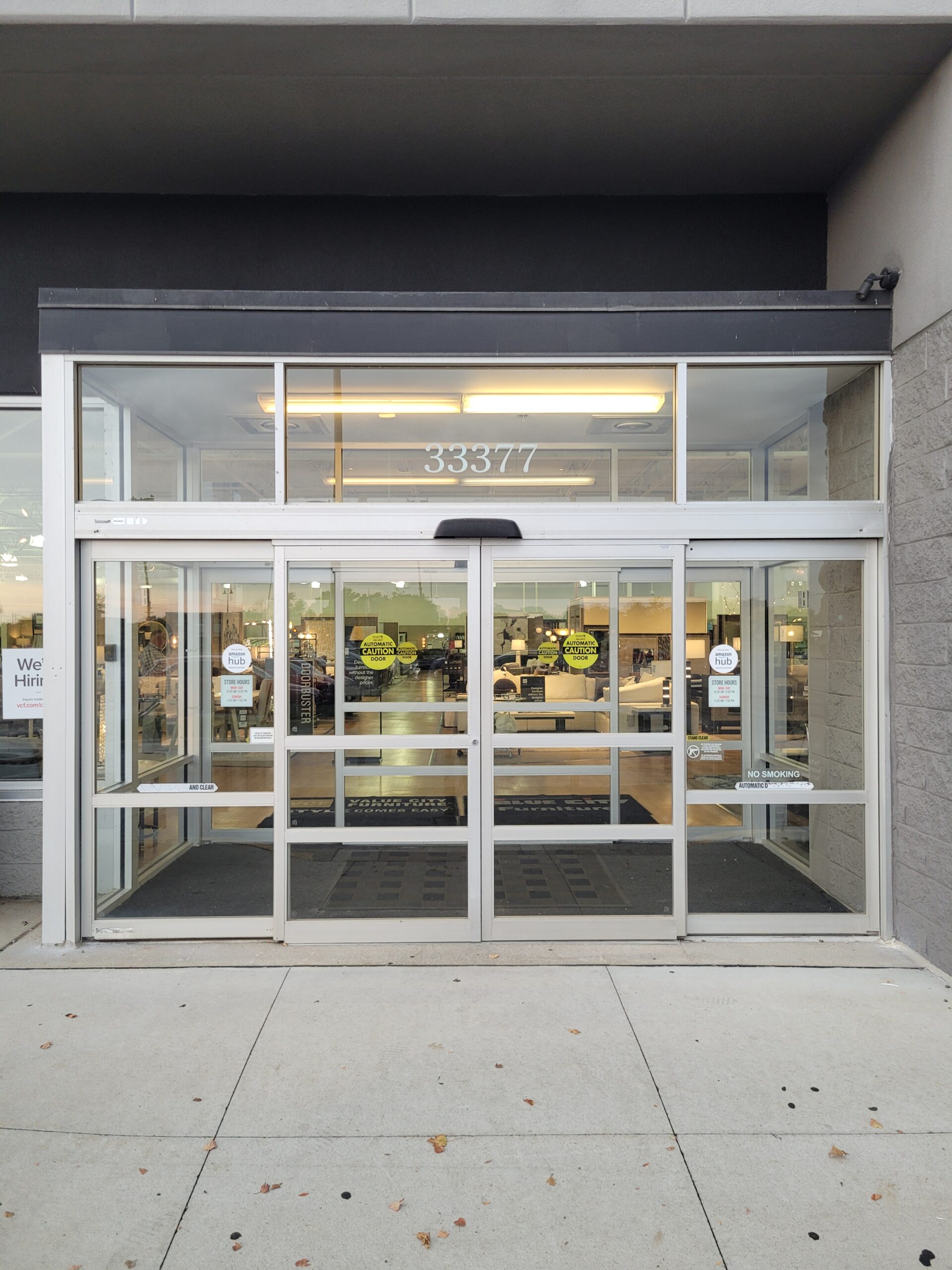 Automatic sliding glass doors at a building entrance with the address number 33377 above; people and checkout counters are visible inside.